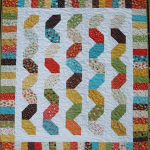 Pode incluir: Uma colcha branca com um padrão em ziguezague feito de retalhos de tecido coloridos. A colcha tem uma borda de listras alternadas de diferentes cores e padrões.