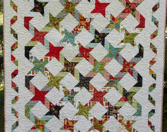 May include: A white quilt with a patchwork design featuring red, green, and black stars. The quilt has a white background with a white border.