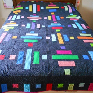 May include: A black quilt with a geometric pattern of colorful stripes. The quilt is made with a variety of colors, including red, orange, yellow, green, blue, purple, and pink. The quilt is laid out on a bed with a white headboard.