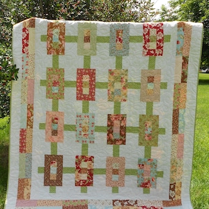 Peut inclure: Une courtepointe faite à la main avec un fond blanc et un motif de grille de blocs rectangulaires dans divers imprimés floraux. Les blocs sont reliés par des lignes vertes, et la courtepointe a une bordure blanche avec des accents floraux.