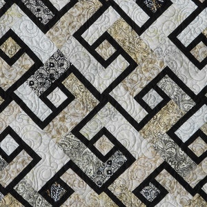 May include: A quilt with a geometric pattern of black squares and rectangles on a background of beige and white fabric with a paisley design.