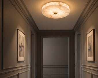 May include: A round, flush-mount ceiling light fixture with a translucent, marbled white and beige stone-like shade. The fixture features a small, centered metallic knob and emits a warm, soft glow, illuminating the surrounding ceiling area.