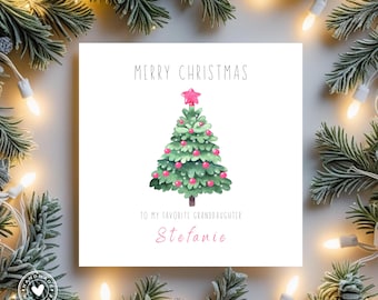May include: A square Christmas card with a watercolor illustration of a Christmas tree, topped with a pink star. The card reads "MERRY CHRISTMAS" and "TO MY FAVORITE GRANDDAUGHTER Stefanie". The card is surrounded by festive greenery and lights.