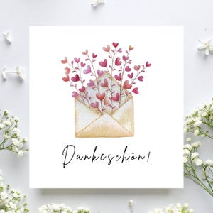 Può includere: Biglietto di auguri quadrato con un'illustrazione ad acquerello di una busta aperta piena di fiori a forma di cuore nei toni del rosa e del rosso. Il biglietto presenta la scritta "Dankeschön!" in corsivo nero.