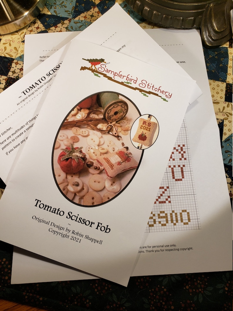 May include: A white paper pattern for a cross stitch project called "Tomato Scissor Fob". The pattern includes a small tomato, scissors, and buttons. The text "RS 2021" is visible in the image.