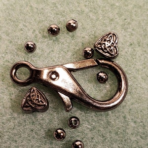 May include: Silver metal clasp with a silver metal heart charm featuring a Celtic knot design. There are also several silver metal beads.
