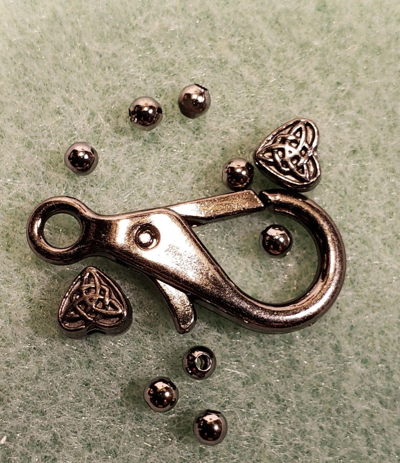 May include: Silver metal clasp with a silver metal heart charm featuring a Celtic knot design. There are also several silver metal beads.