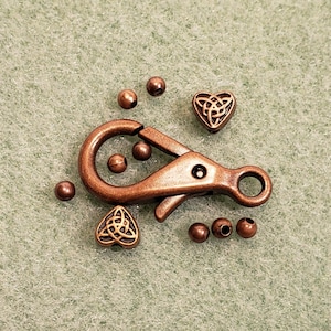 May include: A copper-toned metal clasp with a Celtic knot design, two heart-shaped charms with Celtic knot designs, and several small round beads.
