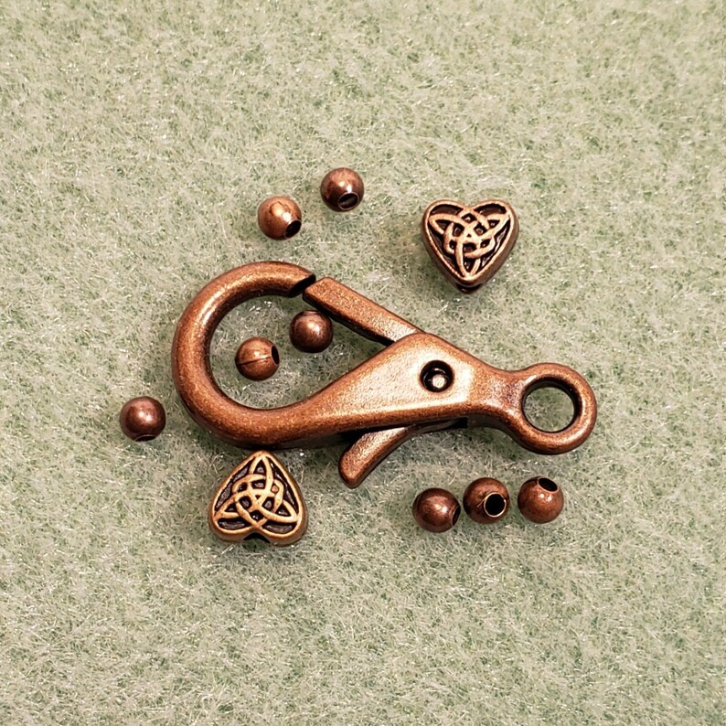 May include: A copper-toned metal clasp with a Celtic knot design, two heart-shaped charms with Celtic knot designs, and several small round beads.