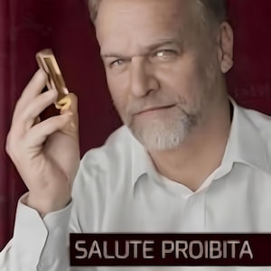 Puede incluir: Un hombre con camisa blanca sostiene un objeto dorado, con el texto "SALUTE PROIBITA" y "INCURABILE ERA IERI" en un rectángulo oscuro. El fondo es rojo oscuro.