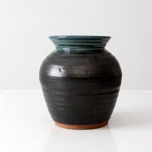 Könnte beinhalten: Eine schwarze Keramikvase mit einem blauen Überzug am Rand. Die Vase hat einen runden Körper und eine leicht ausgestellte Öffnung.