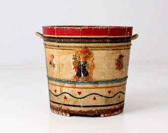 Puede incluir: Un cubo de madera vintage pintado con rayas rojas, verdes y azules y un patrón de corazones. El cubo tiene dos asas de madera y está pintado con una escena de personas en un campo.