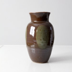 May include: A brown ceramic vase with green accents. The vase has a rounded body and a slightly flared opening.