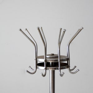 May include: A silver metal coat rack with a circular base and multiple hooks. The rack is designed to hold coats, hats, and other items.