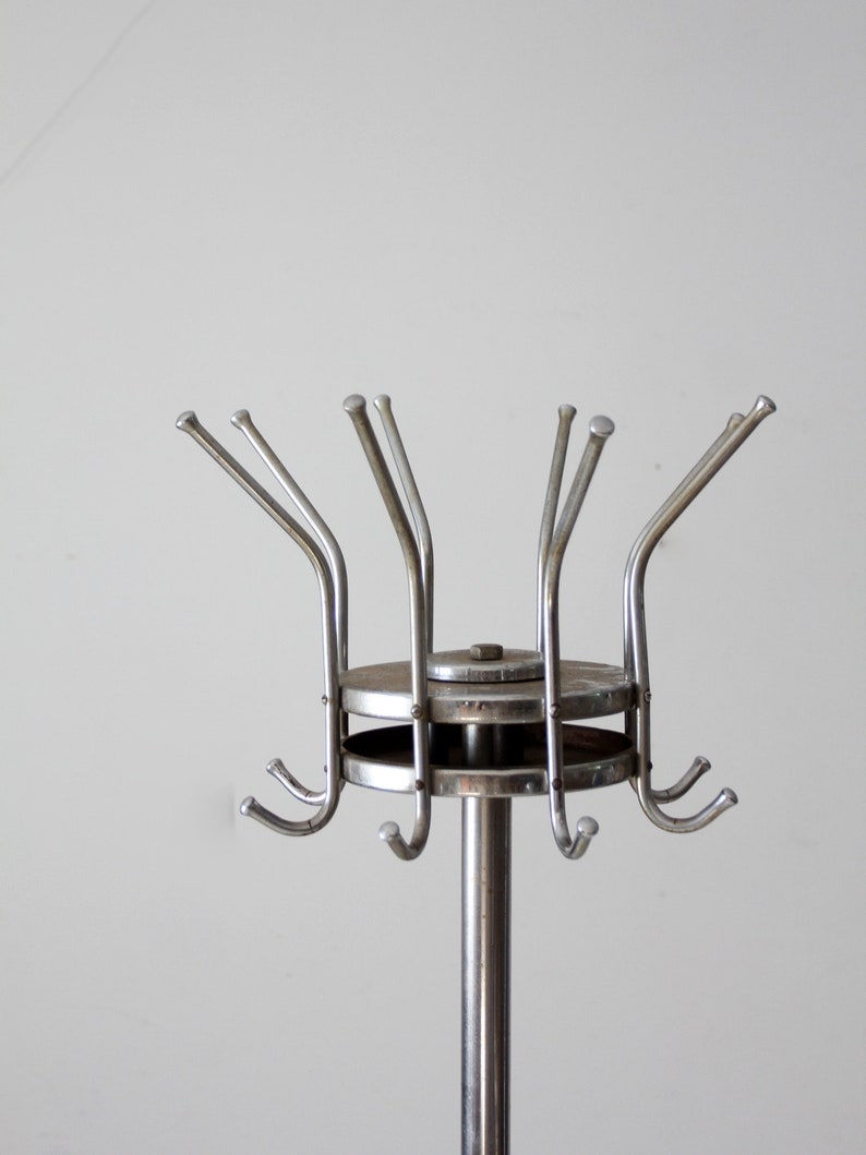 May include: A silver metal coat rack with a circular base and multiple hooks. The rack is designed to hold coats, hats, and other items.
