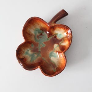 Könnte beinhalten: Eine keramikförmige Schale in Blattform mit brauner, orangefarbener und grüner Glasur. Die Schale hat vier Lappen und einen Stiel, ideal zum Servieren von Snacks oder als dekoratives Stück. Die Glasur hat ein glänzendes Finish.