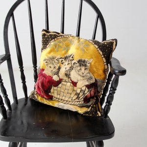 May include: A black wooden chair with a high back and a woven seat. A pillow with a yellow background and a black and white image of three kittens is on the seat.