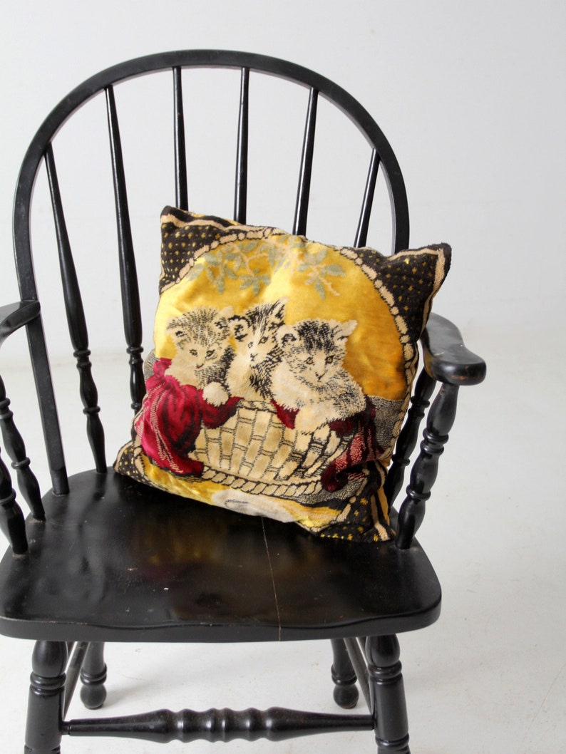 May include: A black wooden chair with a high back and a woven seat. A pillow with a yellow background and a black and white image of three kittens is on the seat.