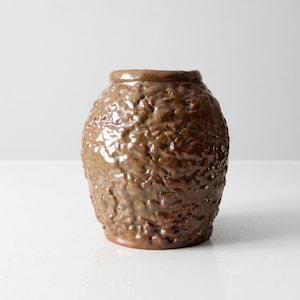 Könnte beinhalten: Eine braune Keramikvase mit einer strukturierten Oberfläche. Die Vase hat eine abgerundete Form und eine breite Öffnung.