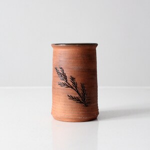 Könnte beinhalten: Eine Terrakotta-Vase mit einem dunkelbraunen Rand und einem einfachen, stilisierten Ast-Design.