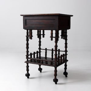 May include: Dark brown antique side table with a rectangular top and a lower shelf. The table features decorative turned legs and small wheels. The wood has a rich, aged appearance, suggesting a vintage piece of furniture.
