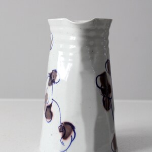 May include: White ceramic pitcher with a blue and brown floral design. The pitcher has a wide mouth and a rounded base.