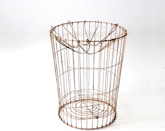 May include: A rusty wire basket with a round base and a cylindrical shape. The basket is made of thin wire and has a rustic, vintage look.