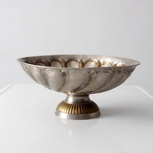 Könnte beinhalten: Silberfarbene Metallschale auf einem Sockel mit gewelltem Rand und geriffelten Seiten. Der Sockel hat eine kontrastierende goldene Farbe mit geripptem Design. Die Schale ist wahrscheinlich Vintage oder antik.