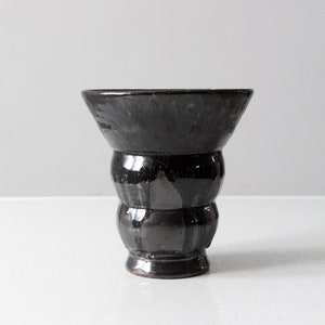 May include: A black ceramic vase with a rounded, bulbous body and a flared opening. The vase has a glossy finish and a slightly textured surface.