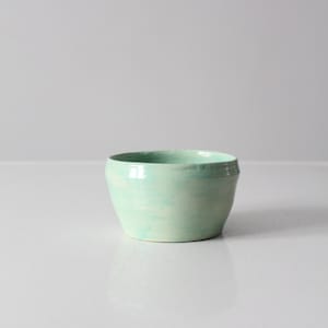 Peut inclure: Un petit bol en céramique de couleur vert clair avec une forme légèrement arrondie. Le bol présente un effet marbré subtil dans le glaçage.