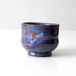 Peut inclure: Une petite tasse en céramique violette avec un motif floral bleu et orange.