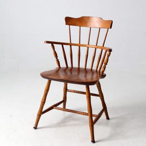 May include: A wooden chair with a spindle back and turned legs. The chair is made of light brown wood and has a simple, classic design.