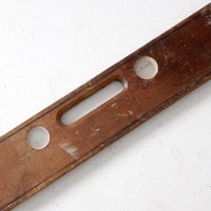 May include: A wooden level with two circular bubble vials. The level is brown and has a handle in the center.