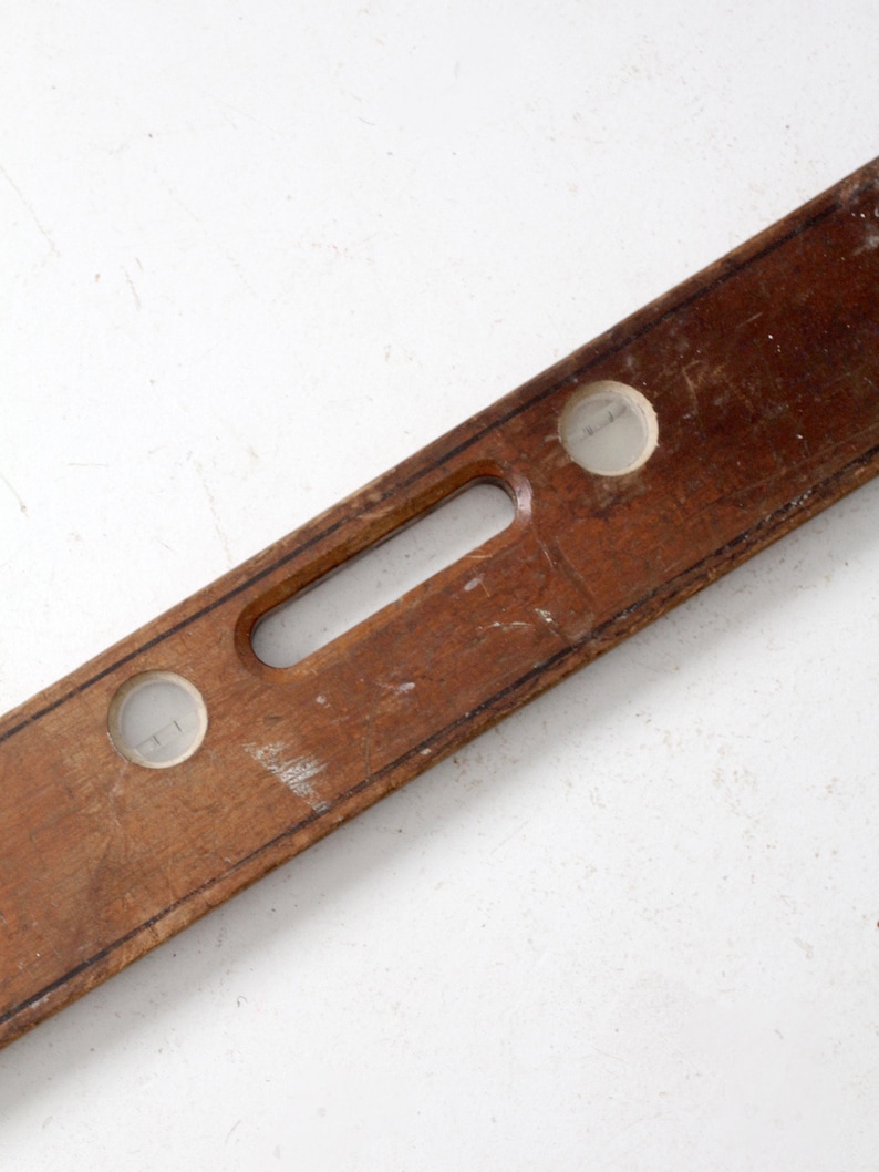 May include: A wooden level with two circular bubble vials. The level is brown and has a handle in the center.