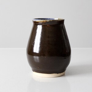 Könnte beinhalten: Eine dunkelbraune Keramikvase mit einem hellbraunen Rand. Die Vase hat eine abgerundete, bauchige Form.