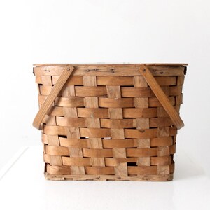 以下が含まれることがあります： 籐製のピクニックバスケット。2つの持ち手と編み込みのデザインが特徴です。ナチュラルな木製のバスケットで、素朴な印象です。