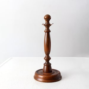 May include: A wooden stand with a round base and a tall, slender column topped with a knob. The column has three small hooks on the top.