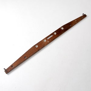 May include: A wooden level with a series of holes and a slot in the center. The level is brown and has a slightly curved shape.