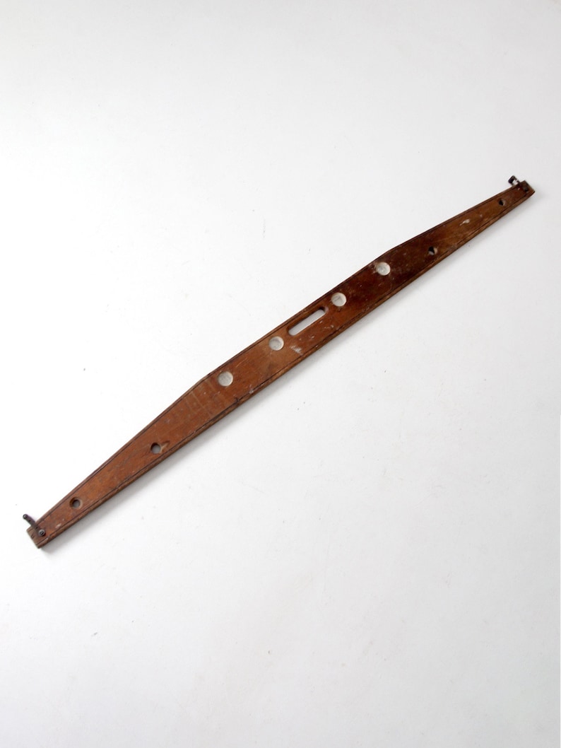 May include: A wooden level with a series of holes and a slot in the center. The level is brown and has a slightly curved shape.