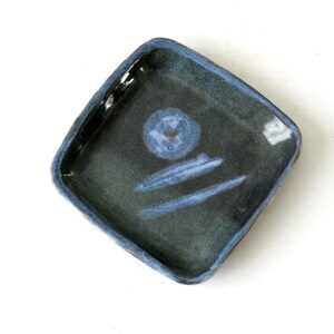 Könnte beinhalten: Eine kleine, quadratische Keramikschale mit blauer Glasur. Die Schale hat einen dunkelblauen Rand und eine hellblaue Mitte mit einem weißen Design.