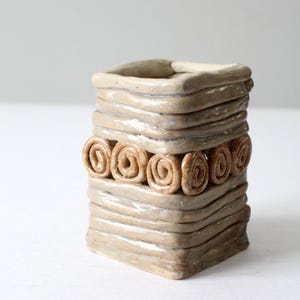 Puede incluir: Un pequeño macetero cuadrado de cerámica con un esmalte marrón claro. El macetero tiene una banda de arcilla marrón en espiral alrededor del medio.