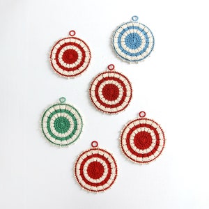 Può includere: Sei ornamenti all'uncinetto in rosso, bianco e blu, verde e bianco e blu. Gli ornamenti sono circolari e hanno un centro bianco con un anello colorato intorno.