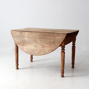 May include: A vintage wooden drop-leaf table with a natural finish. The table features a rectangular top with a rounded drop-leaf and four turned legs. The table is approximately 30 inches long when closed and 48 inches long when open.