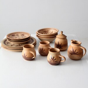 May include: A set of brown pottery dishes with a leaf design. The set includes plates, bowls, mugs, and a creamer.
