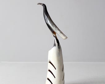 Può includere: Una scultura di uccello bianco e nero in corno. L'uccello è appollaiato su un supporto in corno bianco con dettagli scolpiti.