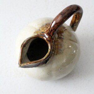 May include: A white ceramic pitcher with a brown handle and a brown glaze. The pitcher has a round body and a spout.