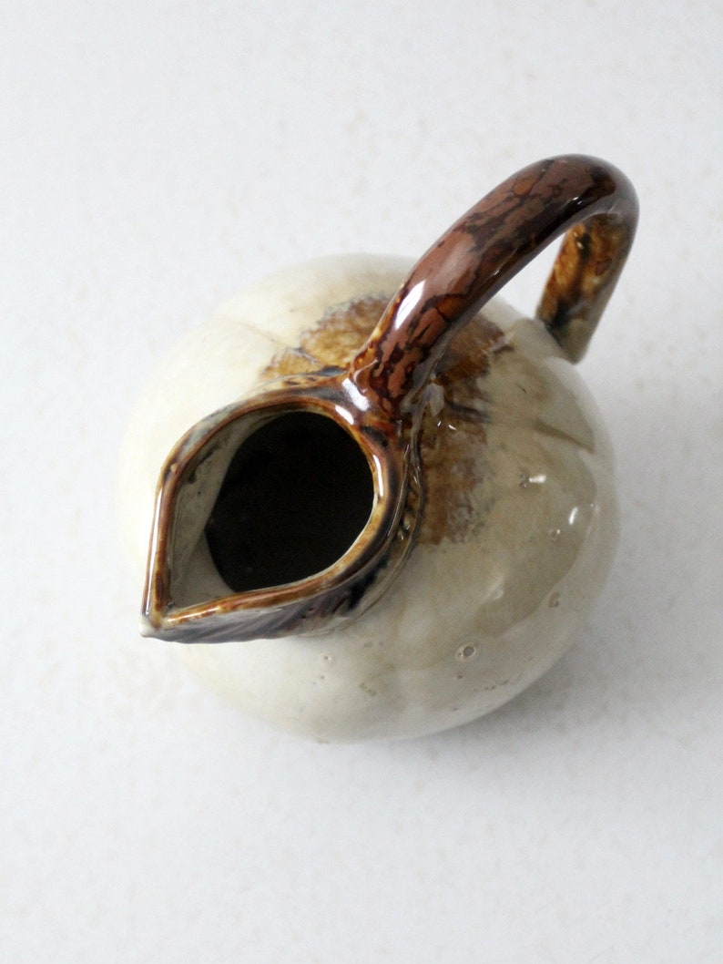 May include: A white ceramic pitcher with a brown handle and a brown glaze. The pitcher has a round body and a spout.