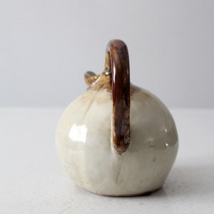 May include: A small, white ceramic pitcher with a brown handle. The pitcher has a rounded body and a slightly flared lip.