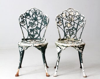 May include: Two white and green metal garden chairs with intricate floral designs. The chairs have a distressed finish and are made of cast iron.