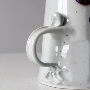 May include: White ceramic pitcher with a speckled glaze and a unique handle. The handle is shaped like a twisted rope and has a small, decorative flower at the base.